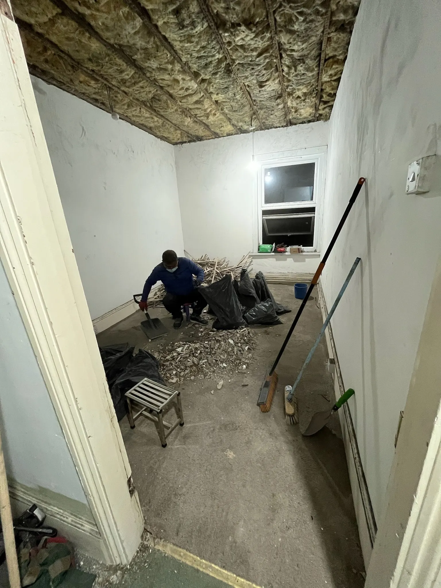 A room in the main house with the ceiling taken down to the insulation, and old laths and plaster being cleared into bags