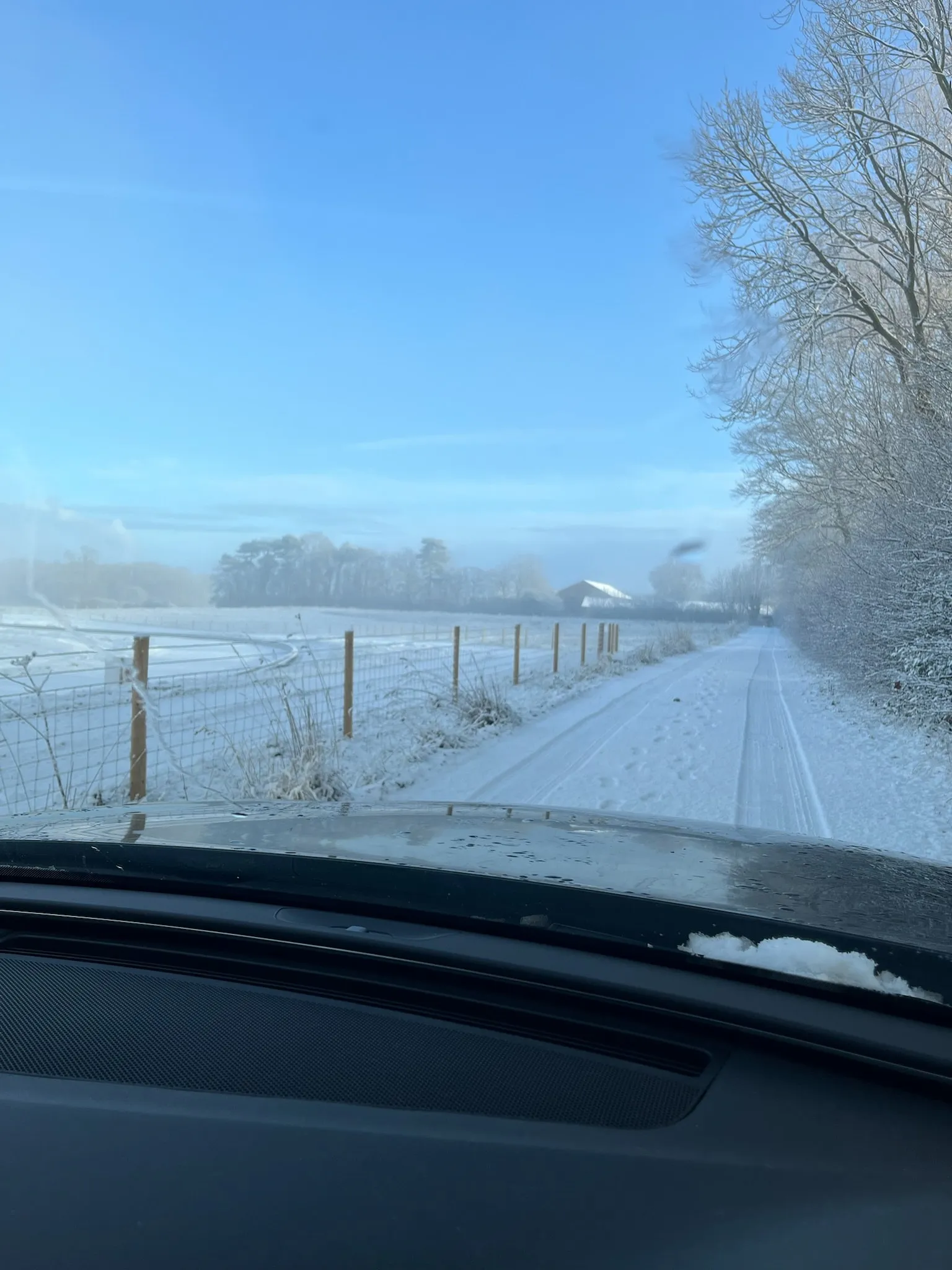 A snow-covered lane beside a fenced field on a clear winter morning